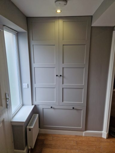 A grey wall with a double door cupboard and a small window beside it.